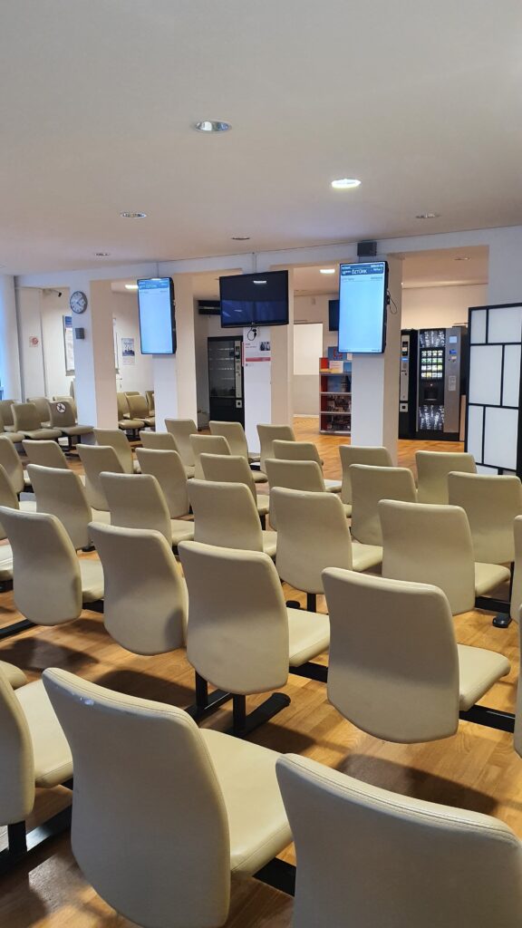 Waiting room with rows of beige chairs and multiple digital queue screens